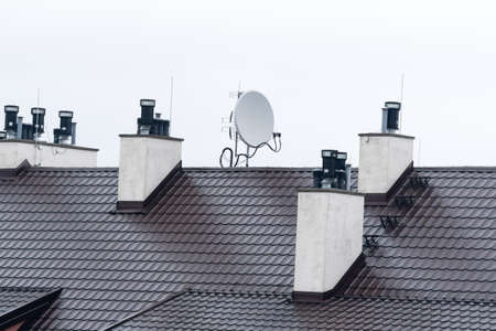 View of the roof of the building with mounted antennas and ventilation pipes against the gray skyの写真素材