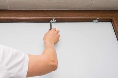 View of a man screwing a screw into a brown plastic window, mounting a blind on a brown plastic windowの写真素材