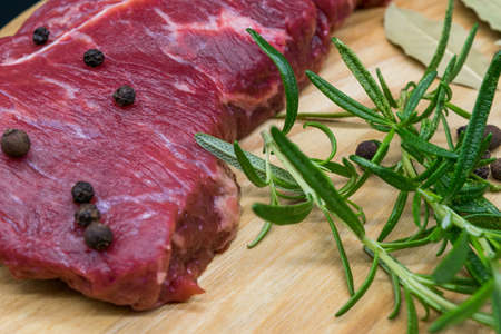 Beef steak, view of fresh beef on a wooden board with rosemary, black pepper, lavatory leaf.の写真素材