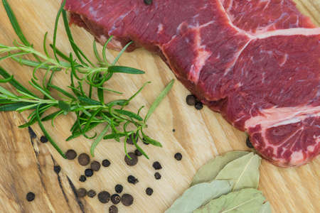 Beef steak, view of fresh beef on a wooden board with rosemary, black pepper, lavatory leaf.