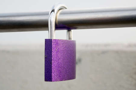 A view of a purple padlock hanging on a metal pipe, close-up viewの写真素材