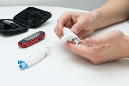 Closeup of young man using lancelet on finger in bathroomの写真素材