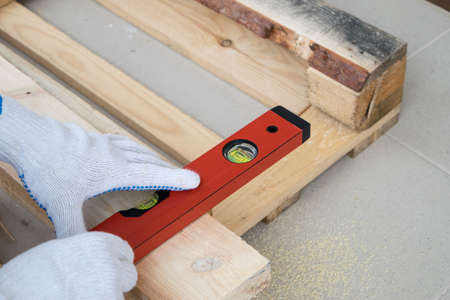 A man in white construction gloves measures a pine board with a tape measure
