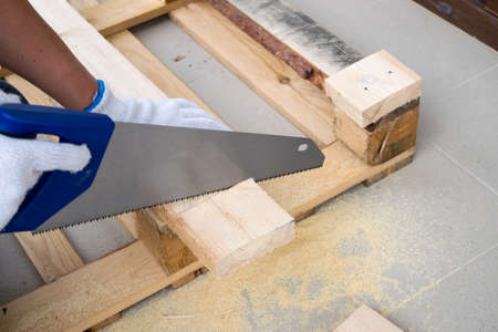 A man in white construction gloves is cutting a wooden plankの写真素材