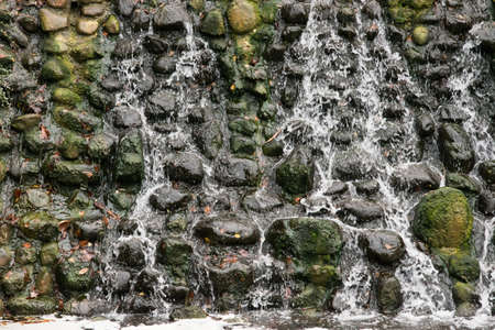 View of a stone wall and water flowing down the wall, a waterfallの写真素材