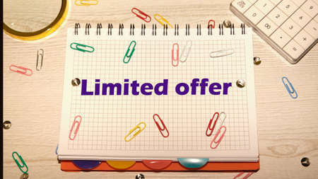 limited offer text on a notebook lying on the table next to a calculator, magnifying glass and paper clips.の写真素材