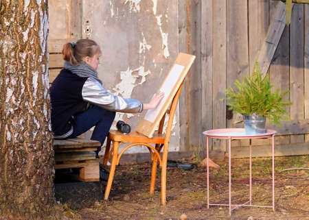 Girl artist paints a picture against the background of an old abandoned house.の写真素材