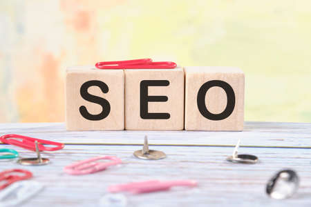 SEO text on wooden cubes next to stationery buttons and paper clips.の写真素材