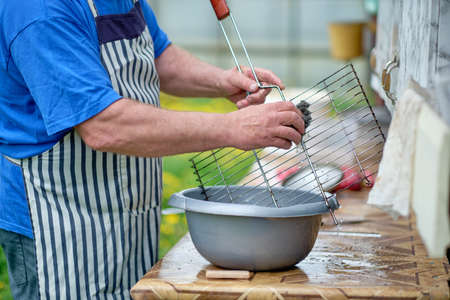 A man washes the grill with a soft sponge. Preparation of the grill for frying meat.の写真素材