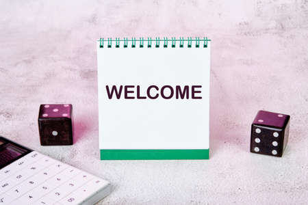 The word WELCOME is written on a notepad, there are dice and a calculator next to it.