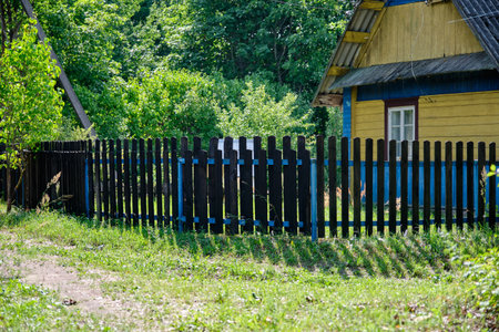An old house surrounded by a wooden fence against a forest backgroundの写真素材