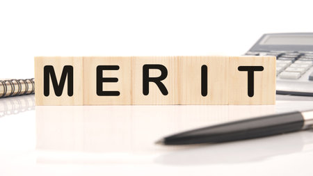 Merit word assembled from wooden cubes next to a calculator, pen and notepadの写真素材