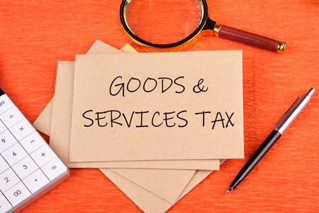Goods and services and tax text written on the envelope next to a magnifying glass, calculator, pen on an orange backgroundの写真素材