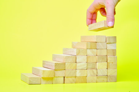 A hand makes a ladder of success out of wooden bars on a yellow backgroundの写真素材
