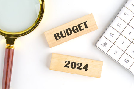 Budget 2024 text on wooden blocks on a white background next to a calculator and a magnifying glass