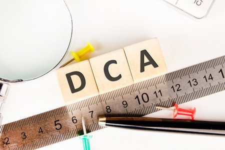 Dollar cost averaging DCA text on wooden cubes near a measuring ruler, magnifying glass, calculator.の写真素材
