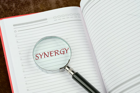 Synergy, cooperation or efficiency in business concept. The word synergy through a magnifying glass in the notebook of a businessman, manager, teacherの写真素材