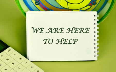 WE ARE HERE TO HELP CONCEPT on a notepad on the background of a clock next to a calculator
