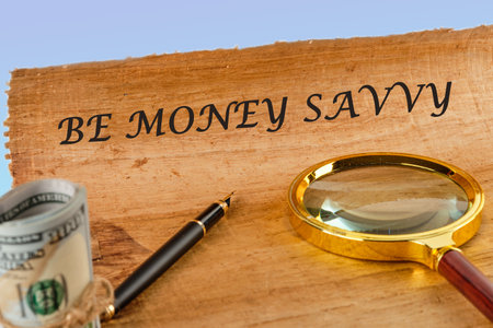 Savings concept,Text Be money savvy on papyrus next to a magnifying glass and money