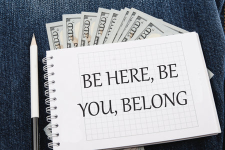 BE HERE, BE YOU, BELONG Words written on a notebook lying on jeans with dollar bills