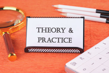 Business, theory and practice concept. Copy space. Words 'Theory and practice' on a white business card in a stand with a magnifying glass, pencils and a calculatorの写真素材