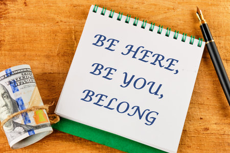 BE HERE, BE YOU, BELONG Words written on a notepad near money and a fountain pen on an abstract backgroundの写真素材