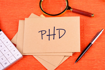 Word PhD. on postal envelopes in a composition with a calculator, magnifying glass and pen on an...