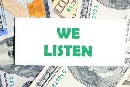 WE LISTEN written on a white business card against a background of dollar bills