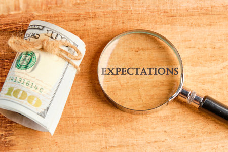 inscription Expectations word through a magnifying glass with American dollars lying next to it