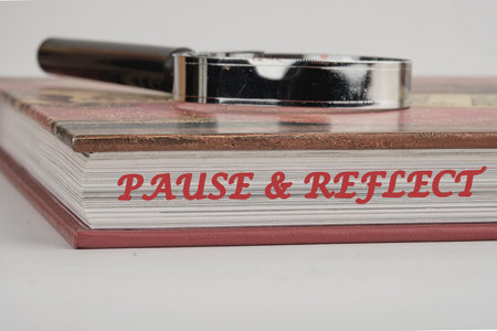 Pause and reflect word on the end of the book with a magnifying glass on top on a white background