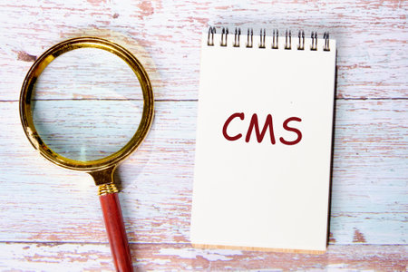Business concept. CMS - short for Content Management System in a notebook next to a magnifying glass...