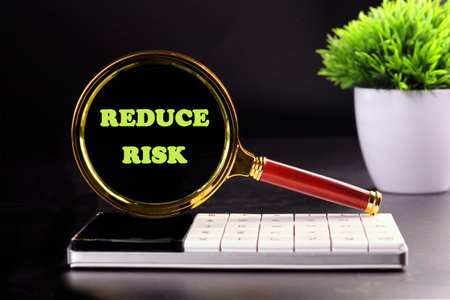 Conceptual reduce risk symbol. Copy space. Words REDUCE RISK through a magnifying glass on a calculator on a black backgroundの写真素材
