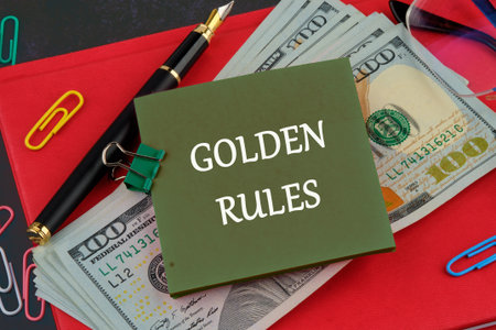 Conceptual golden rule symbol. Copy space. GOLDEN RULES words on a green sticker on the background of American dollars and a red business bookの写真素材