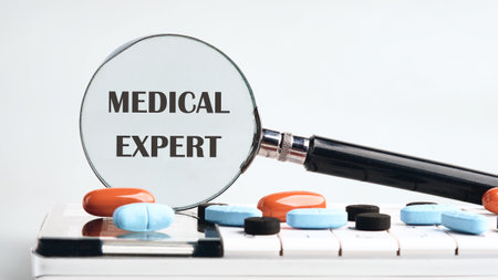 Concept word MEDICAL EXPERT Medicine and MEDICAL EXPERT concept. Copy space. MEDICAL EXPERT symbol through a magnifying glass on a calculator with tablets on a gray background. The concept of medicineの写真素材