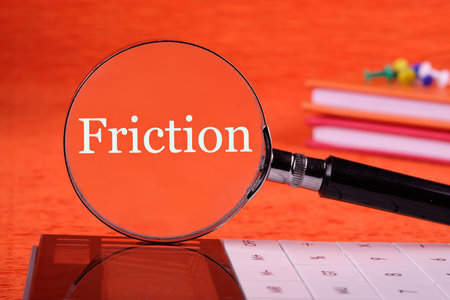 Friction concept. Friction word through a magnifying glass standing vertically on a calculator on an orange background, front viewの写真素材