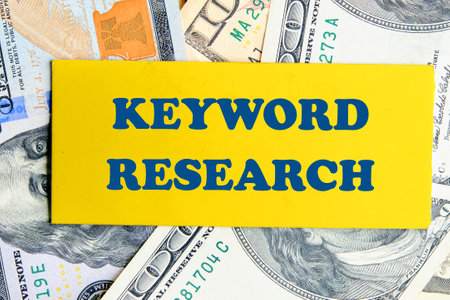 KEYWORD RESEARCH written a conceptual phrase on a yellow business card against the background of American dollarsの写真素材