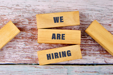 Business and Now Hiring concept. Copy space. Words WE ARE HIRING on wooden blocks close-up from aboveの写真素材