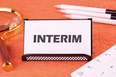 Interim writing on a white business card, close-up in front of an orange background, front viewの写真素材