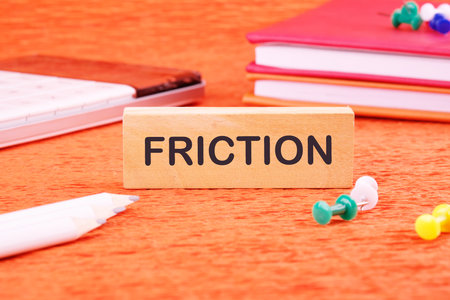 Friction concept. Friction word on a wooden bar in front of an orange background, front viewの写真素材