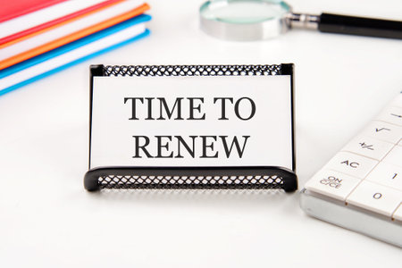 Conceptual time to renew concept. Copy space. Time to renew words written on a business card in a composition with a magnifying glass, notebooks, a calculator on a white backgroundの写真素材