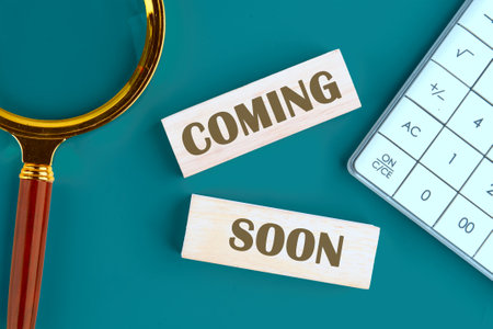 Coming soon text written it is laid out from wooden blocks , top view in a composition with a calculator and a magnifying glassの写真素材