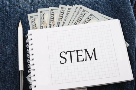 STEM word and symbols on a checkered notebook against the background of American paper bills