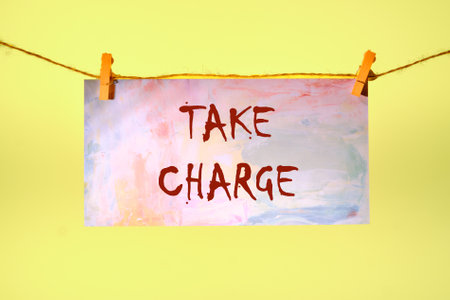 Conceptual take charge symbol. Copy space. TAKE CHARGE words written on a piece of paper in a clothespin on a rope on a yellow backgroundの写真素材