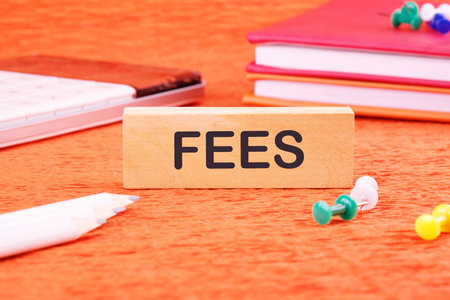 Business and finance concept. Costs, charges, commissions, penalties. Cost, fee and taxes. FEES on a wooden bar in front of an orange background, front viewの写真素材