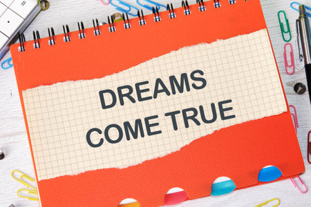 Conceptual dreams come true symbol. Copy space. Dreams come true words on a piece of paper in a cage on the background of a notebookの写真素材
