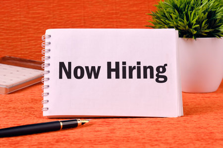 Business and Now Hiring concept. Copy space. Now Hiring on a blank notepad page on an orange backの写真素材