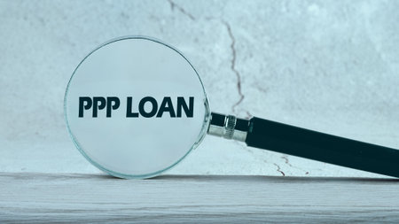 Paycheck Protection Program PPP Loan written through a magnifying glass on a gray background