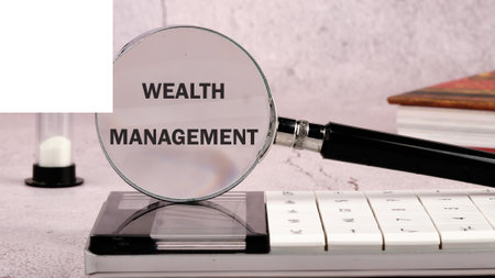 WEALTH MANAGEMENT words written through a magnifying glass on a gray background in a composition with a calculator, an hourglass and a bookの写真素材