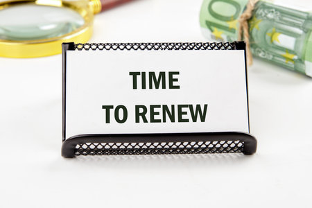 Conceptual time to renew concept. Copy space. Time to renew words written on a business card on a white background with a magnifying glass in the backgroundの写真素材