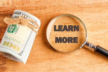 LEARN MORE text through a magnifying glass on papyrus next to dollar billsの写真素材